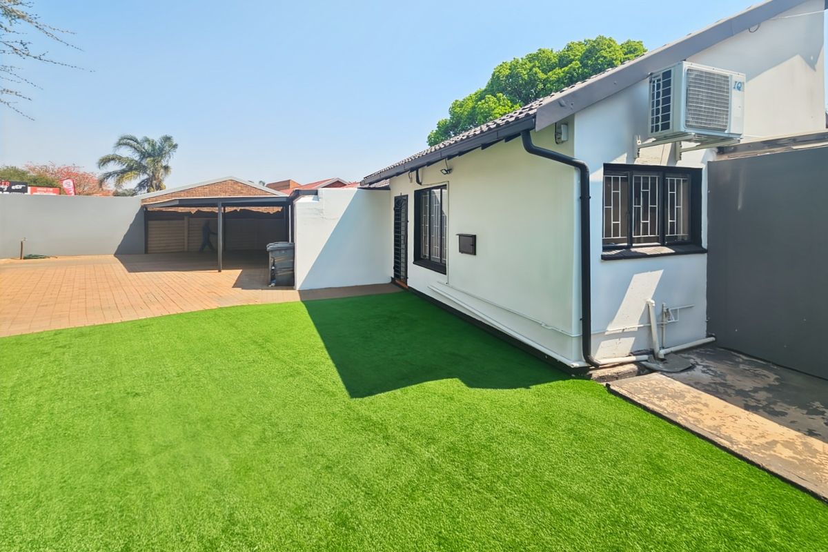 Rear view of the property featuring a low-maintenance artificial lawn, paved driveway, and a covered carport area.