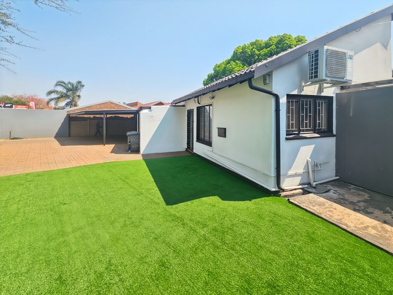 Rear view of the property featuring a low-maintenance artificial lawn, paved driveway, and a covered carport area.