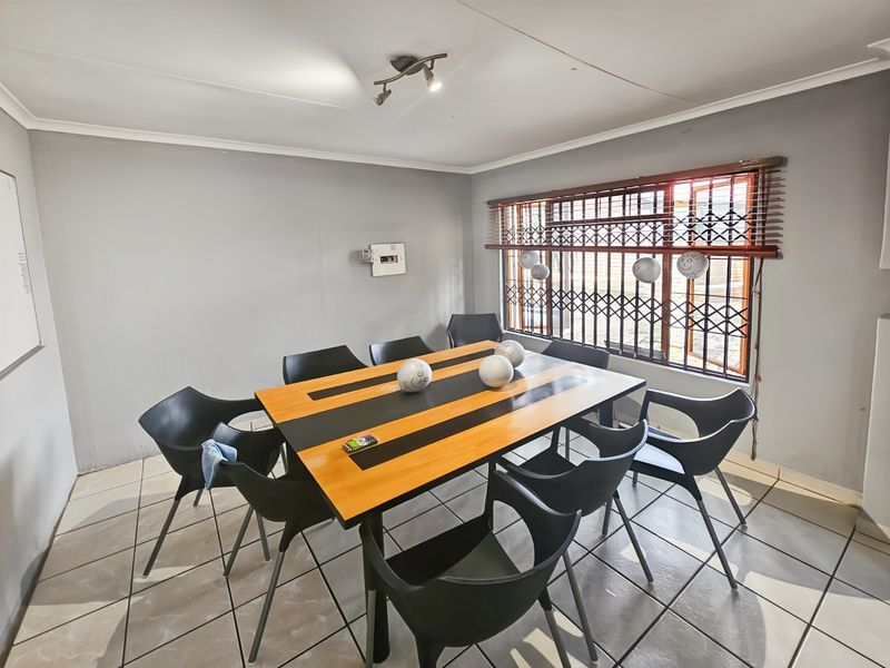 A functional dining room featuring tiled flooring, a window with security bars and blinds, and a wall-mounted electrical distribution board.
