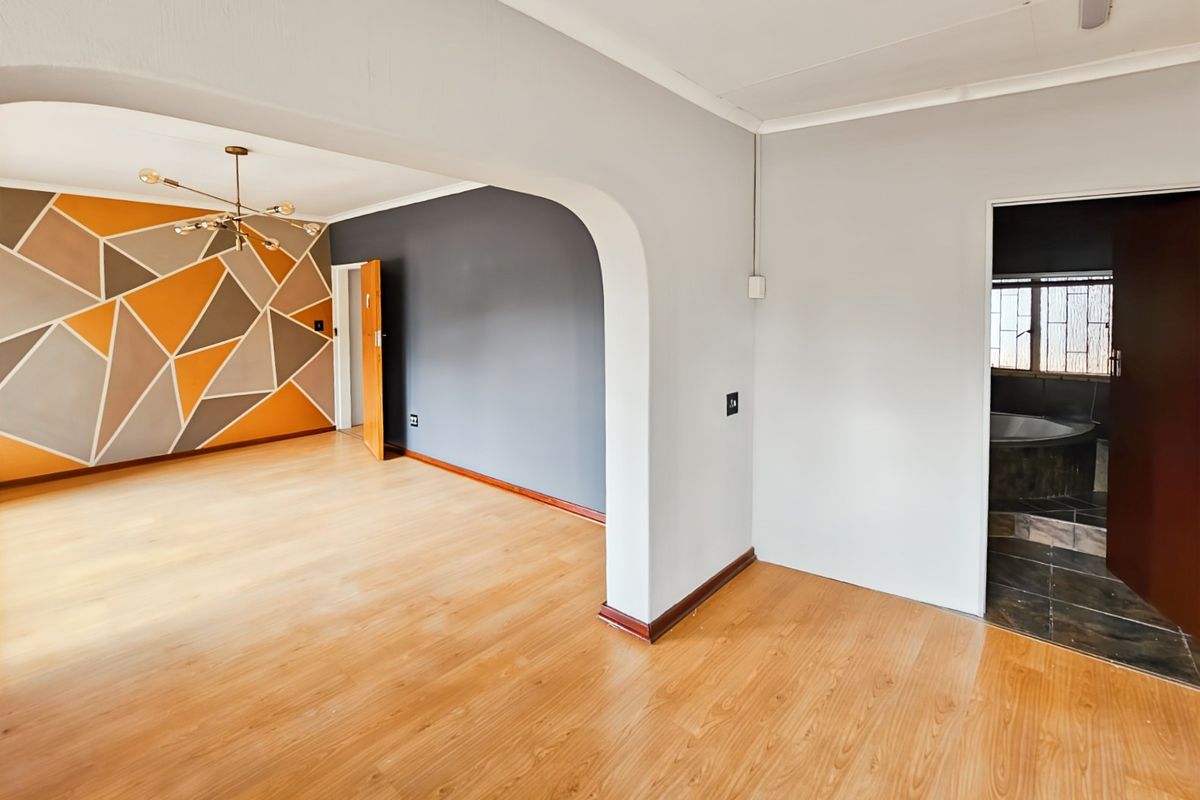 Spacious living area featuring laminate flooring, a decorative archway, and a modern geometric accent wall, leading into an adjacent room.