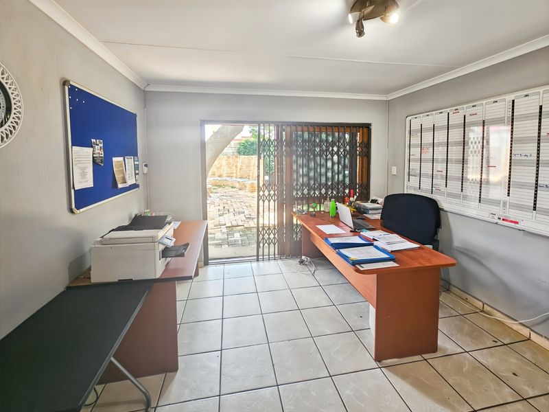 A functional home office space featuring tiled flooring, a sliding glass door with security gate, and direct access to the outdoor area.