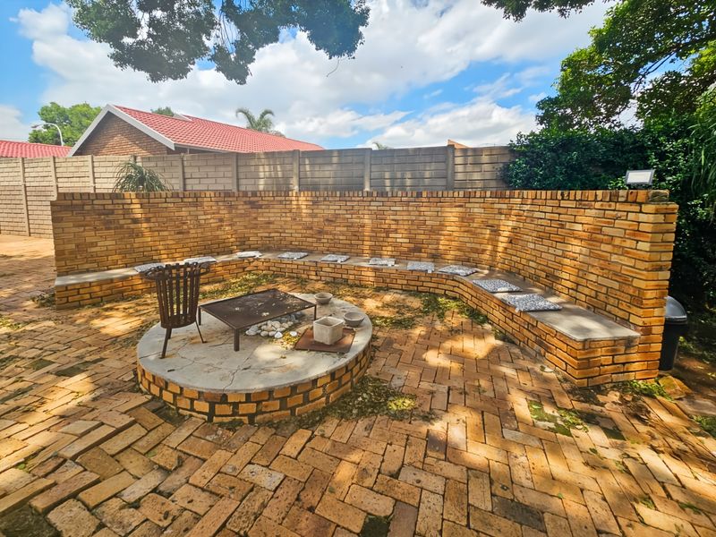 Outdoor entertainment area featuring a circular brick fire pit with integrated curved bench seating and paved flooring, enclosed by a brick boundary wall.