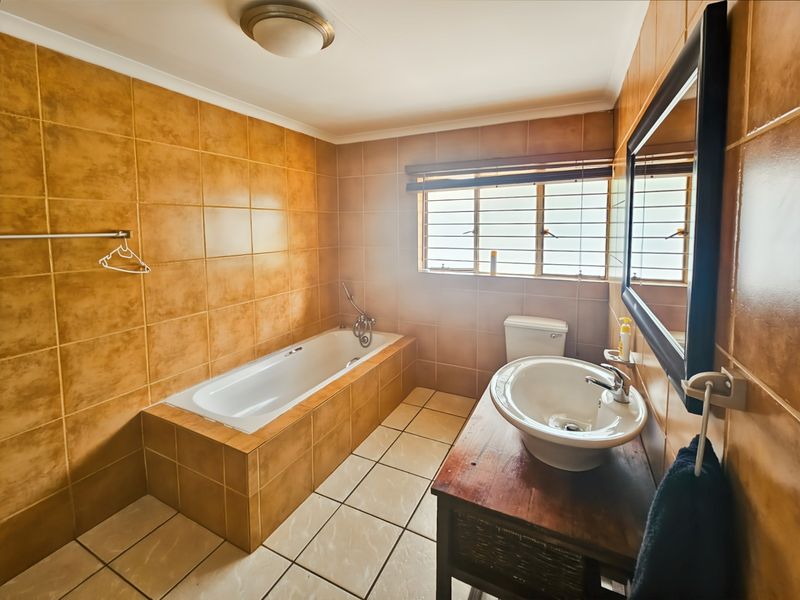 A functional bathroom featuring a built-in bathtub, vessel sink vanity, and full-height ceramic wall tiling with a window for natural light.