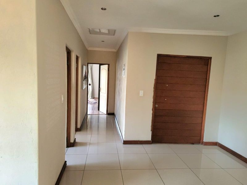 A bright, tiled hallway featuring recessed downlights and a wooden door, providing access to multiple rooms within the home.