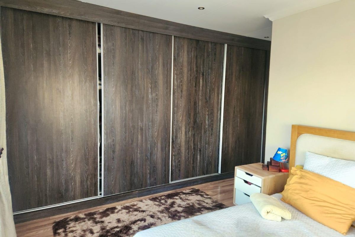 A bedroom featuring dark wood-grain built-in sliding door wardrobes and laminate flooring, providing ample storage space.
