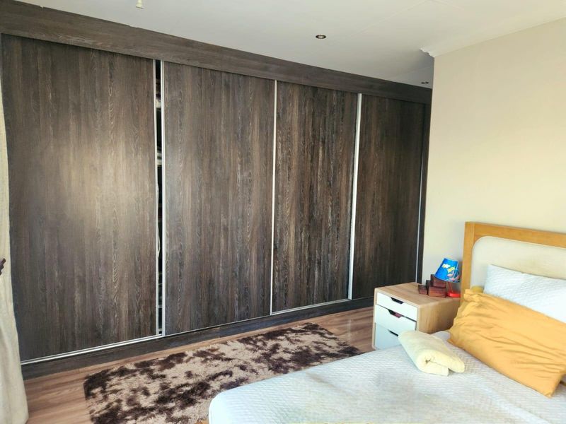 A bedroom featuring dark wood-grain built-in sliding door wardrobes and laminate flooring, providing ample storage space.