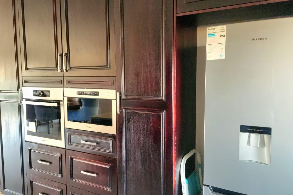A kitchen section featuring dark wood cabinetry with integrated built-in oven and microwave units alongside a dedicated refrigerator housing space.