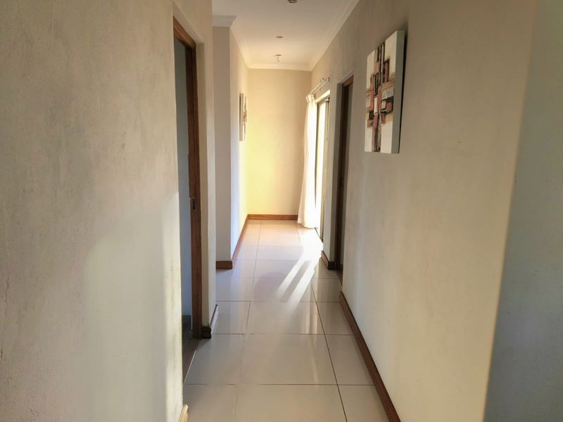 A bright, tiled hallway connecting multiple rooms, featuring neutral wall tones and recessed lighting.