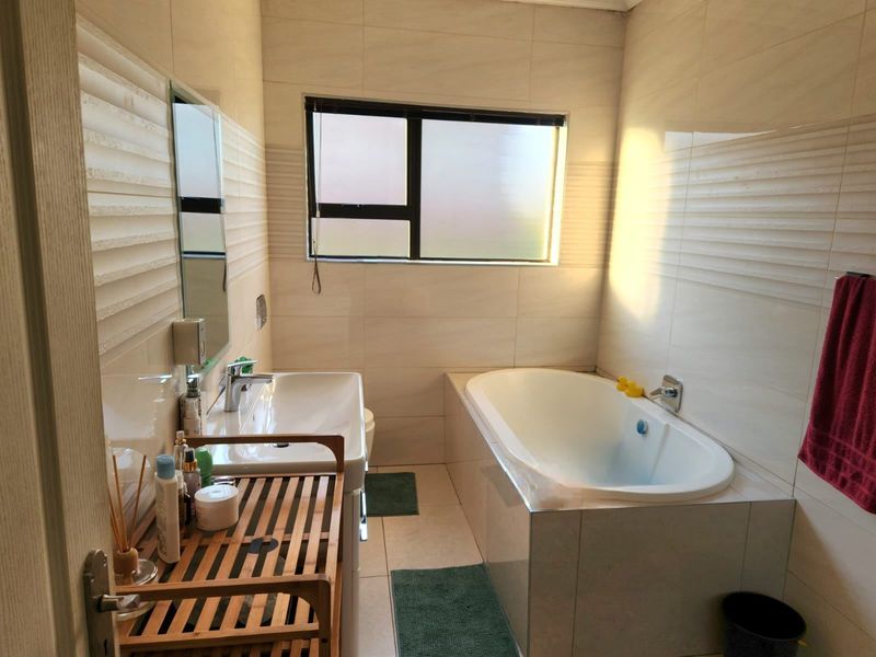 A well-maintained bathroom featuring a built-in bathtub, wall-mounted basin, and modern tiled finishes with natural light from a frosted window.