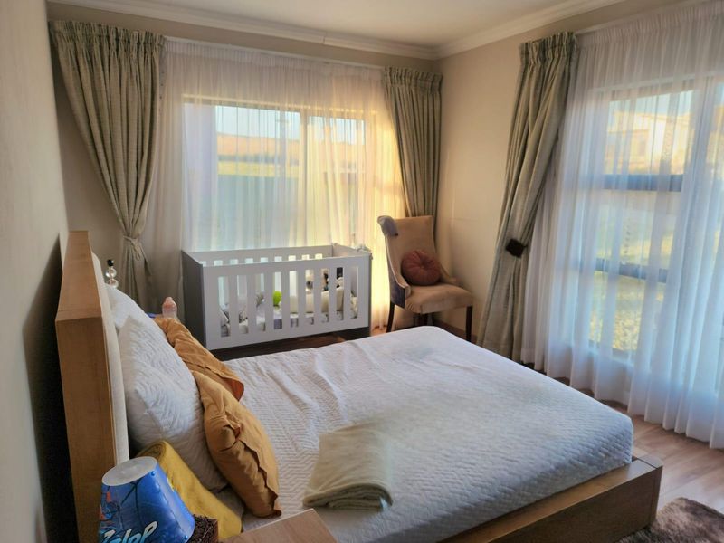 A well-lit bedroom featuring laminate flooring, large sliding windows with curtain tracks, and neutral wall finishes.