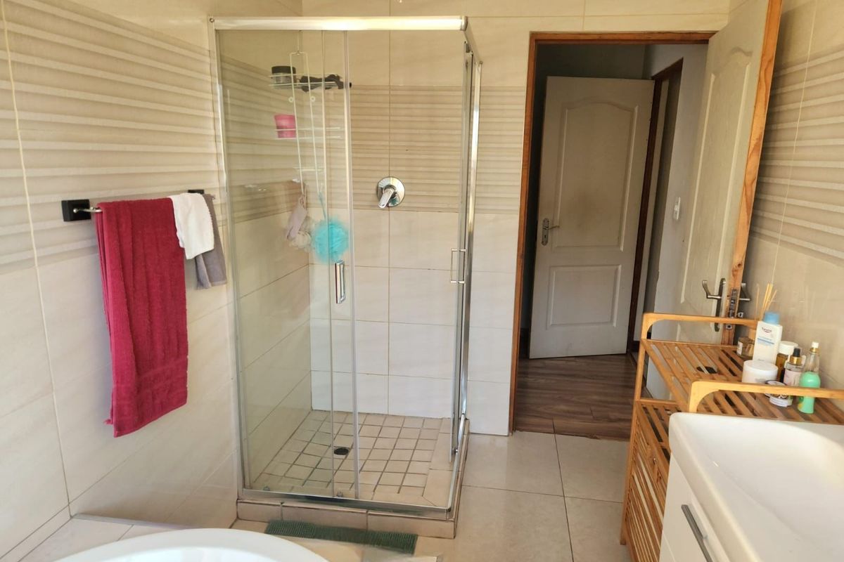 A functional bathroom featuring a glass-enclosed shower, neutral wall tiling, and tiled flooring, providing a clean and practical space.