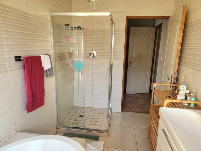 A functional bathroom featuring a glass-enclosed shower, neutral wall tiling, and tiled flooring, providing a clean and practical space.