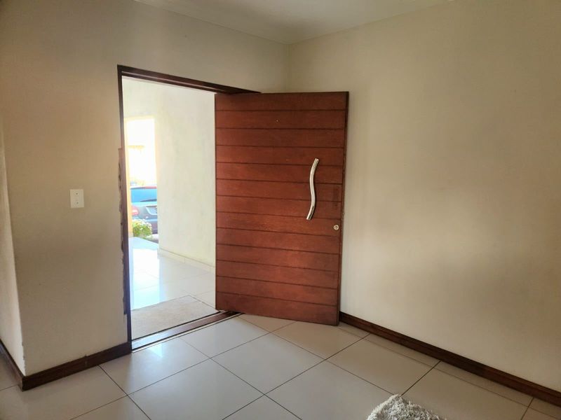 An empty entry area featuring a large wooden pivot door and neutral ceramic floor tiles, providing a clean canvas for interior design.