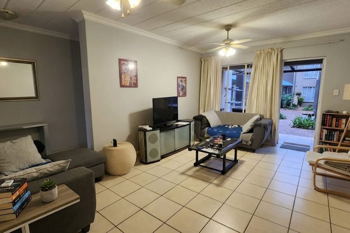 A comfortable living room featuring ceramic floor tiles, crown molding, and a sliding glass door providing access to an outdoor patio area.