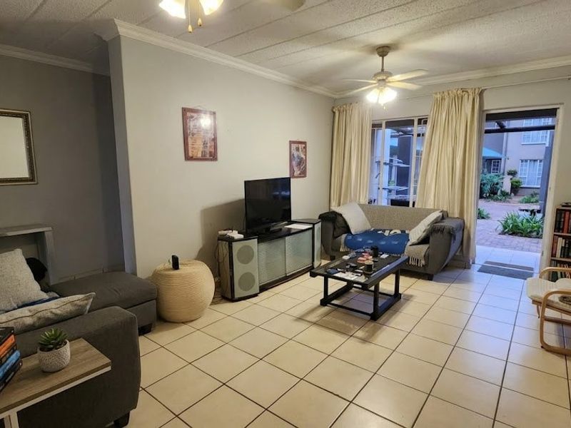 A comfortable living room featuring ceramic floor tiles, crown molding, and a sliding glass door providing access to an outdoor patio area.