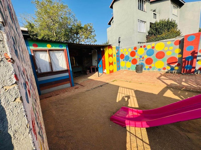Rear outdoor area featuring a paved patio, covered section, and boundary walls with decorative paintwork, offering potential for landscaping and renovation.