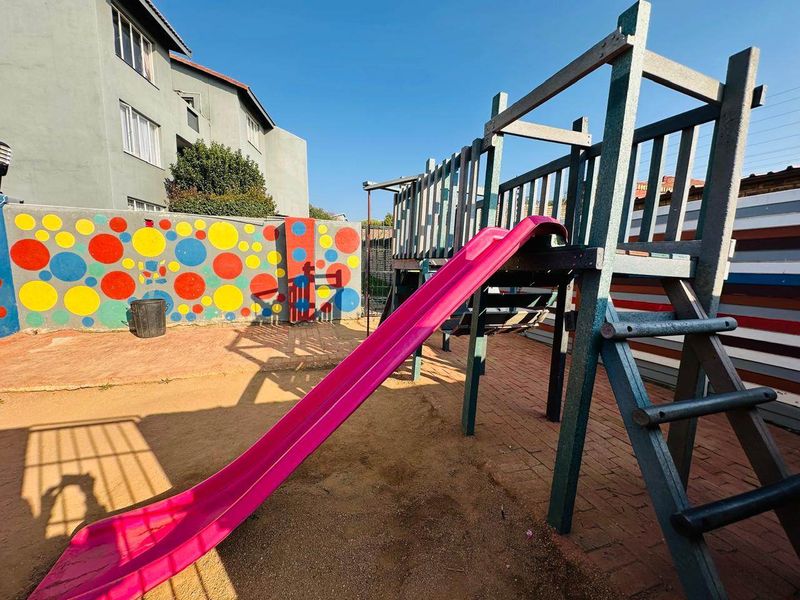 Rear outdoor area featuring a playground structure with a slide and a decorative painted boundary wall.