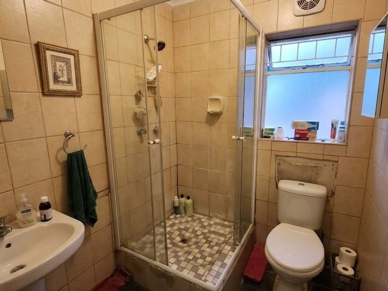 Compact bathroom featuring a shower enclosure, pedestal basin, and toilet, with floor-to-ceiling wall tiling and an integrated extractor fan.