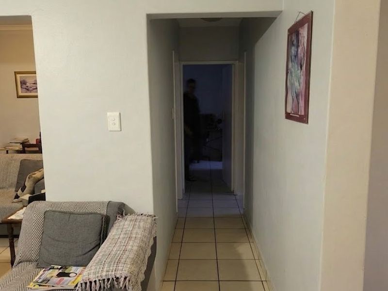 A view through a central hallway connecting living areas, featuring neutral wall finishes and tiled flooring throughout.