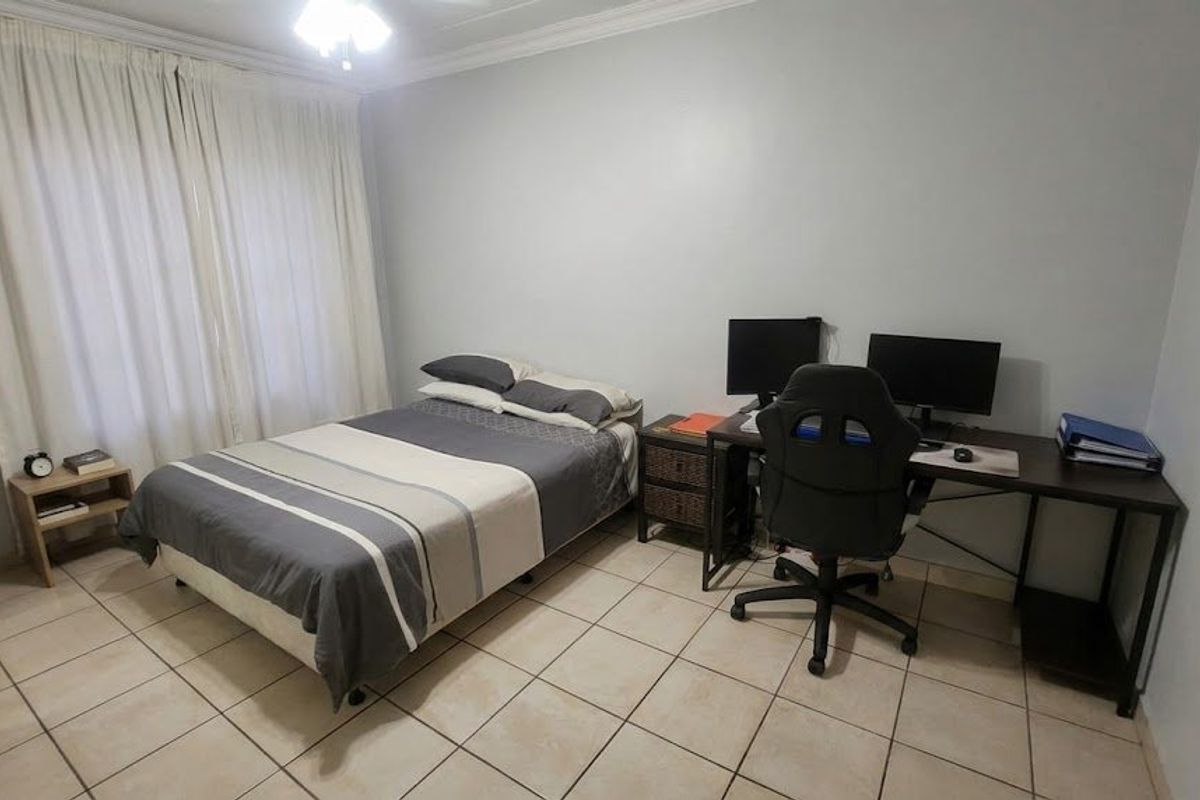 A functional bedroom featuring tiled flooring, neutral wall finishes, and large windows with curtains, suitable for use as a sleeping area or home office.