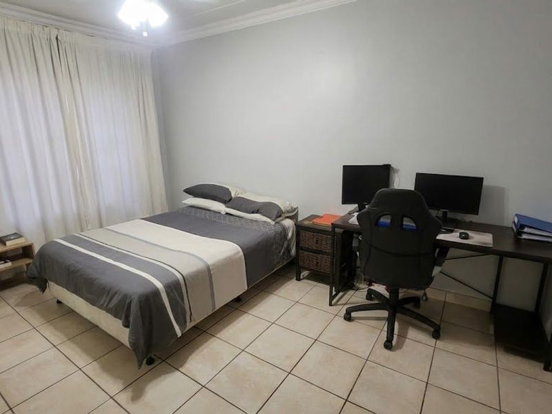 A functional bedroom featuring tiled flooring, neutral wall finishes, and large windows with curtains, suitable for use as a sleeping area or home office.