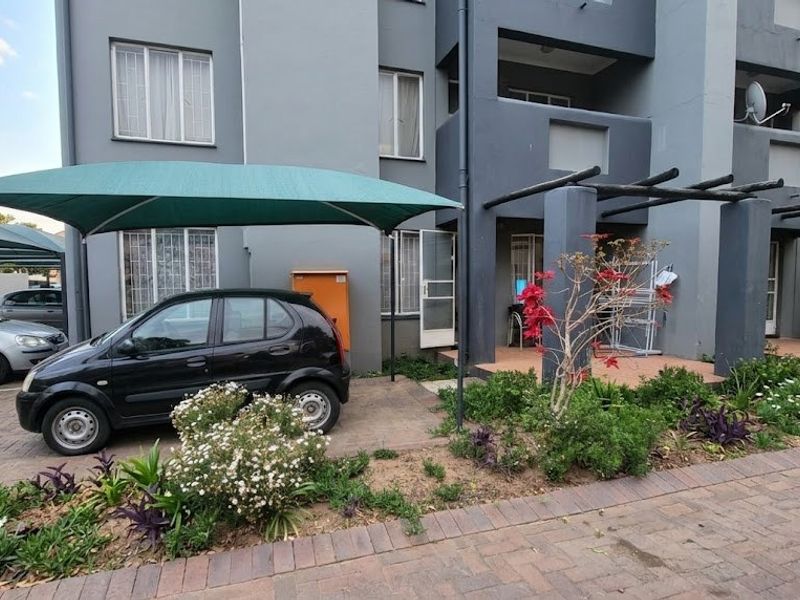 Front exterior view of the apartment building featuring a paved driveway, shade cloth carport, and a small landscaped garden area.