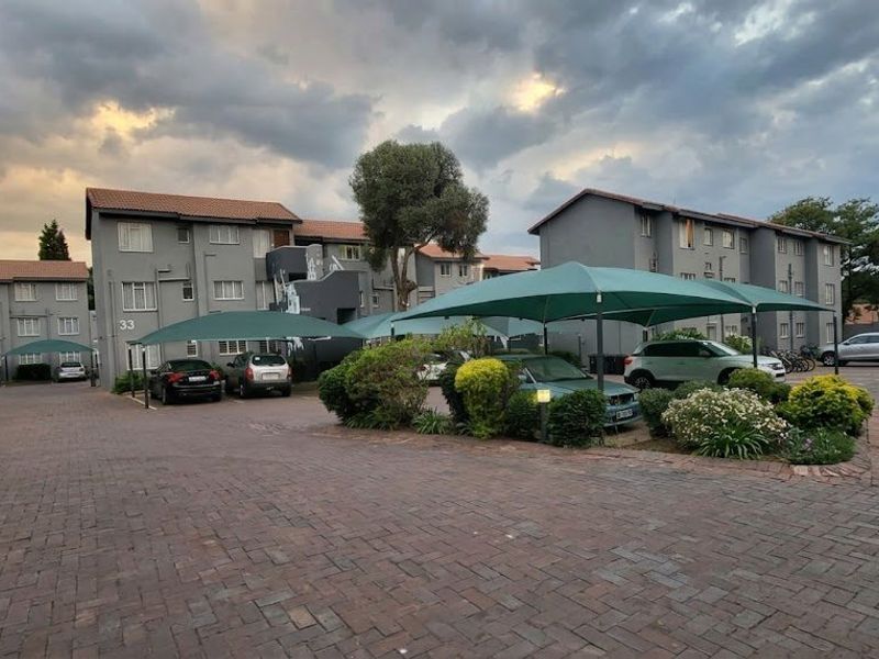Exterior view of an apartment complex featuring paved parking areas with shade cloth carports and established garden landscaping.