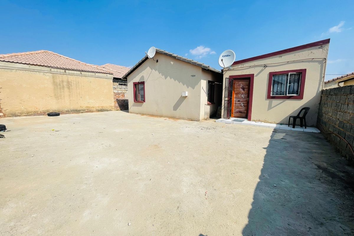 Rear exterior view of the property featuring a large concrete yard, perimeter walling, and a tiled roof structure.
