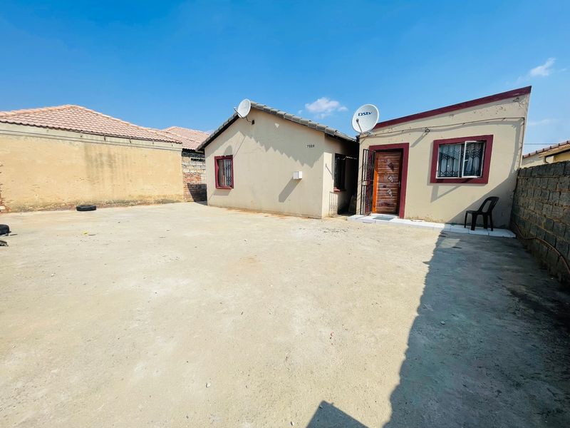 Rear exterior view of the property featuring a large concrete yard, perimeter walling, and a tiled roof structure.