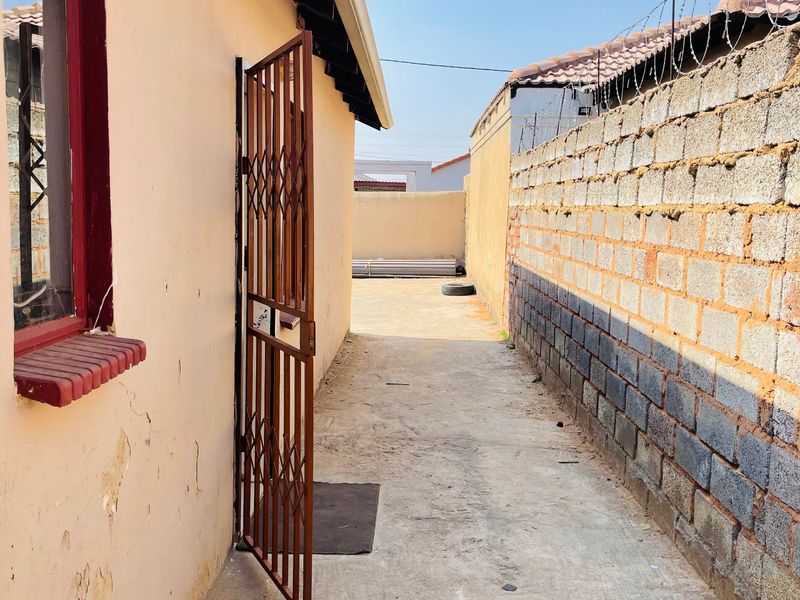 A narrow rear exterior walkway featuring concrete paving, a security gate, and a perimeter wall topped with razor wire.