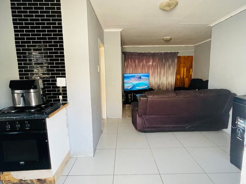 Open plan living area featuring tiled flooring and a kitchen section with a built-in oven and black tiled splashback.