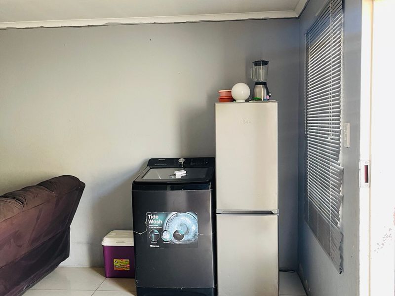 A functional laundry area featuring tiled flooring and venetian blinds, currently housing utility appliances. The space requires minor cosmetic updates to improve its overall finish.