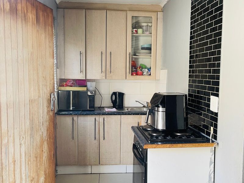 Compact kitchen featuring light wood cabinetry, black subway tile backsplash, gas stove, and tiled flooring, requiring minor finishing touches to complete the space.