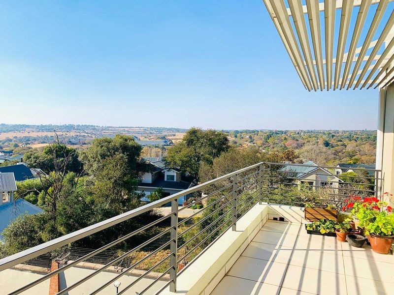 Spacious balcony featuring a modern metal balustrade, tiled flooring, and a slatted pergola, offering expansive elevated views of the surrounding landscape.