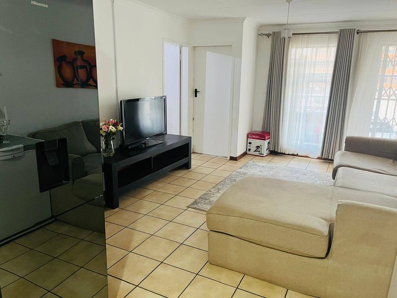 A bright living room featuring tiled flooring and a sliding glass door with security gate, providing access to the exterior.
