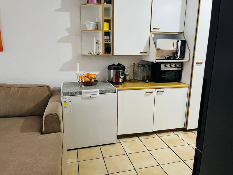 A compact kitchen area featuring white cabinetry, laminate countertops, and tiled flooring, integrated into an open-plan living space.