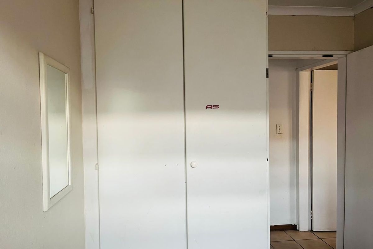 A bedroom featuring built-in cupboards and tiled flooring, requiring minor cosmetic updates to refresh the space.
