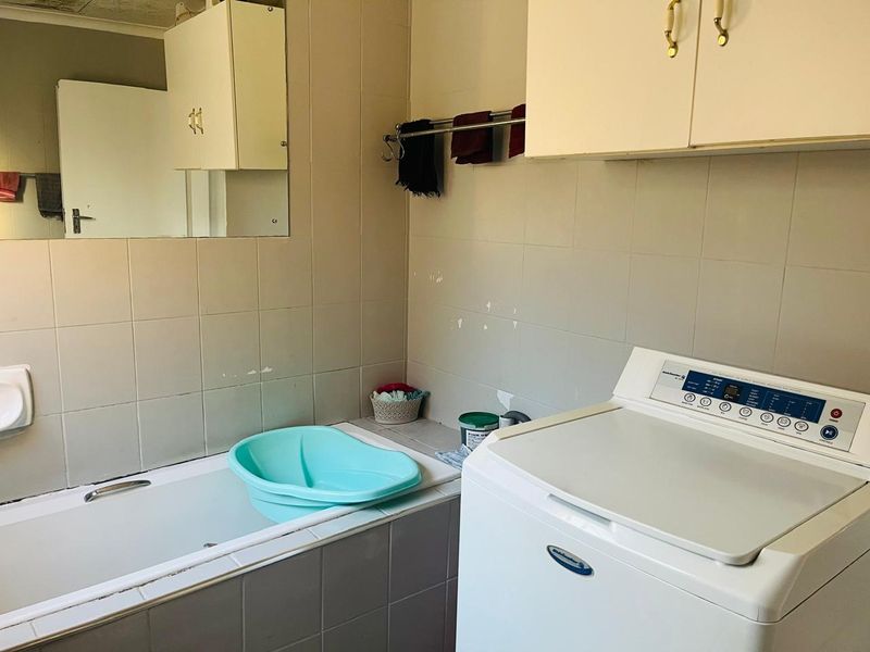 A functional laundry area featuring built-in cabinetry, a tiled bathtub, and wall-mounted storage, offering potential for modernization and improved utility space design.