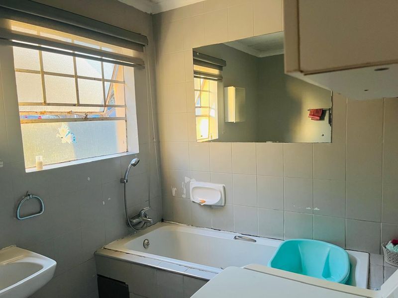 A dated bathroom featuring a bathtub with handheld shower, wall-mounted basin, and tiled walls, requiring cosmetic updates to improve its overall condition.