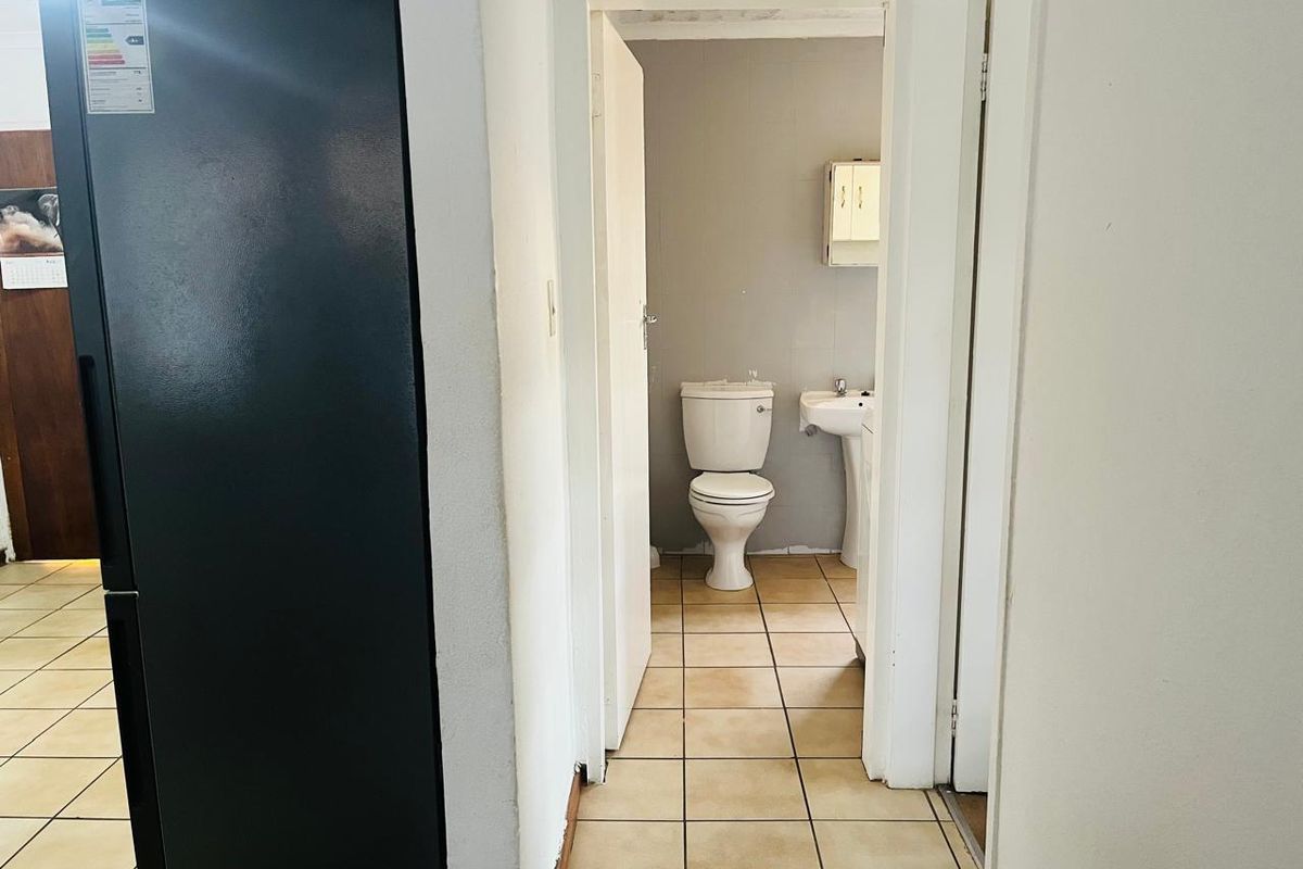 A small bathroom featuring a pedestal basin, toilet, and tiled flooring, accessible via a hallway.
