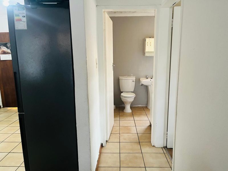 A small bathroom featuring a pedestal basin, toilet, and tiled flooring, accessible via a hallway.