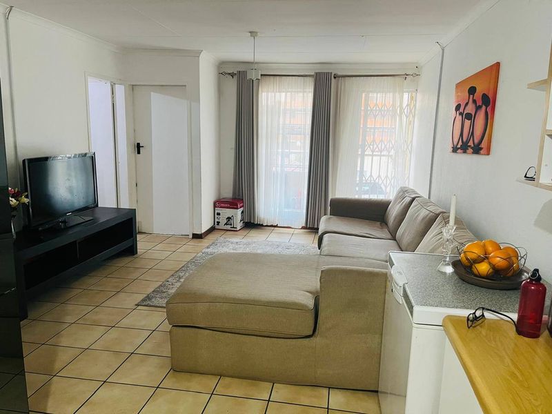 A functional living room featuring tiled flooring and a sliding glass door with a security gate, providing access to the exterior.