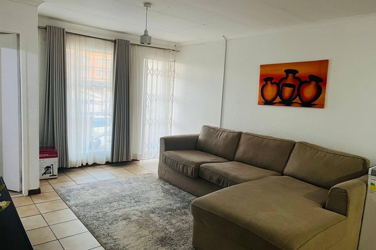 A living room featuring tiled flooring and a sliding glass door with security gate, providing access to the exterior.