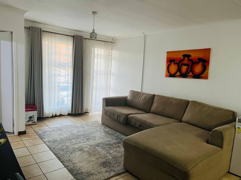 A living room featuring tiled flooring and a sliding glass door with security gate, providing access to the exterior.