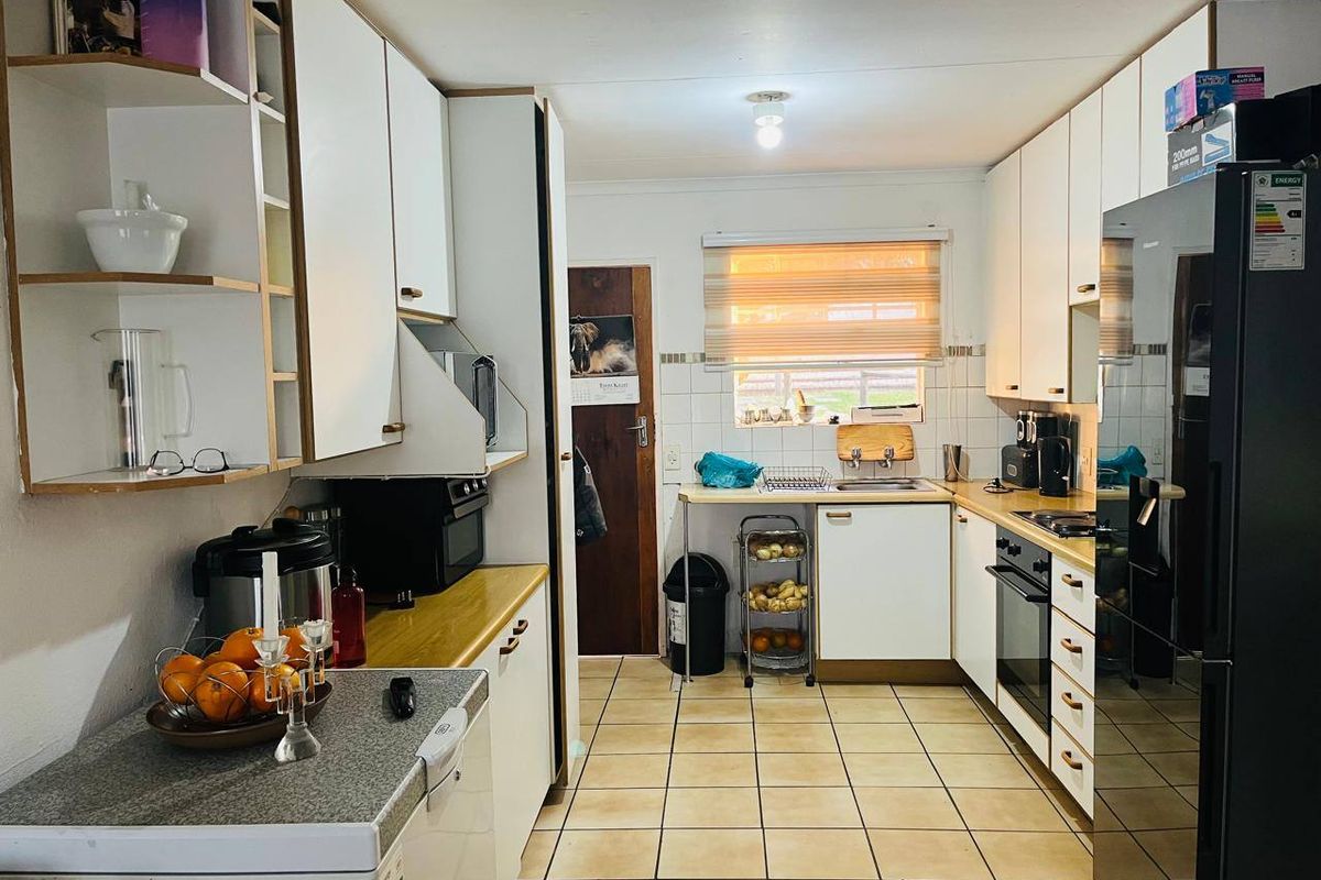 A functional galley-style kitchen featuring white cabinetry, laminate countertops, tiled flooring, and a built-in oven and hob.