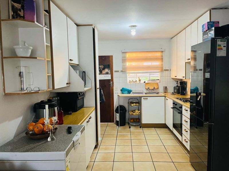 A functional galley-style kitchen featuring white cabinetry, laminate countertops, tiled flooring, and a built-in oven and hob.