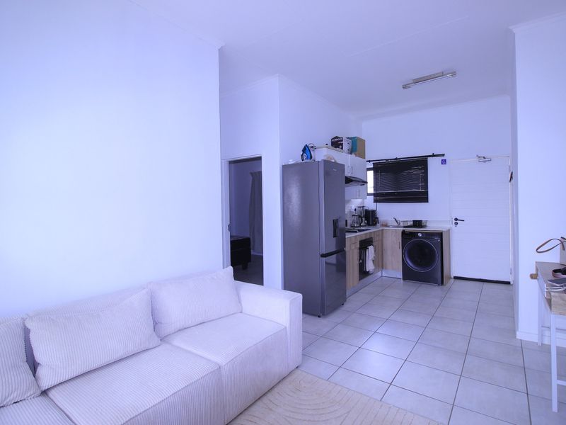 Open-plan living area featuring tiled flooring and a compact kitchen with built-in cabinetry, hob, and extractor fan.