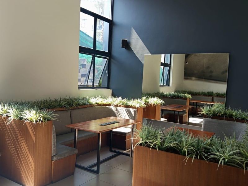A modern living area featuring built-in bench seating, integrated planters, a large wall mirror, and tiled flooring with natural light from casement windows.