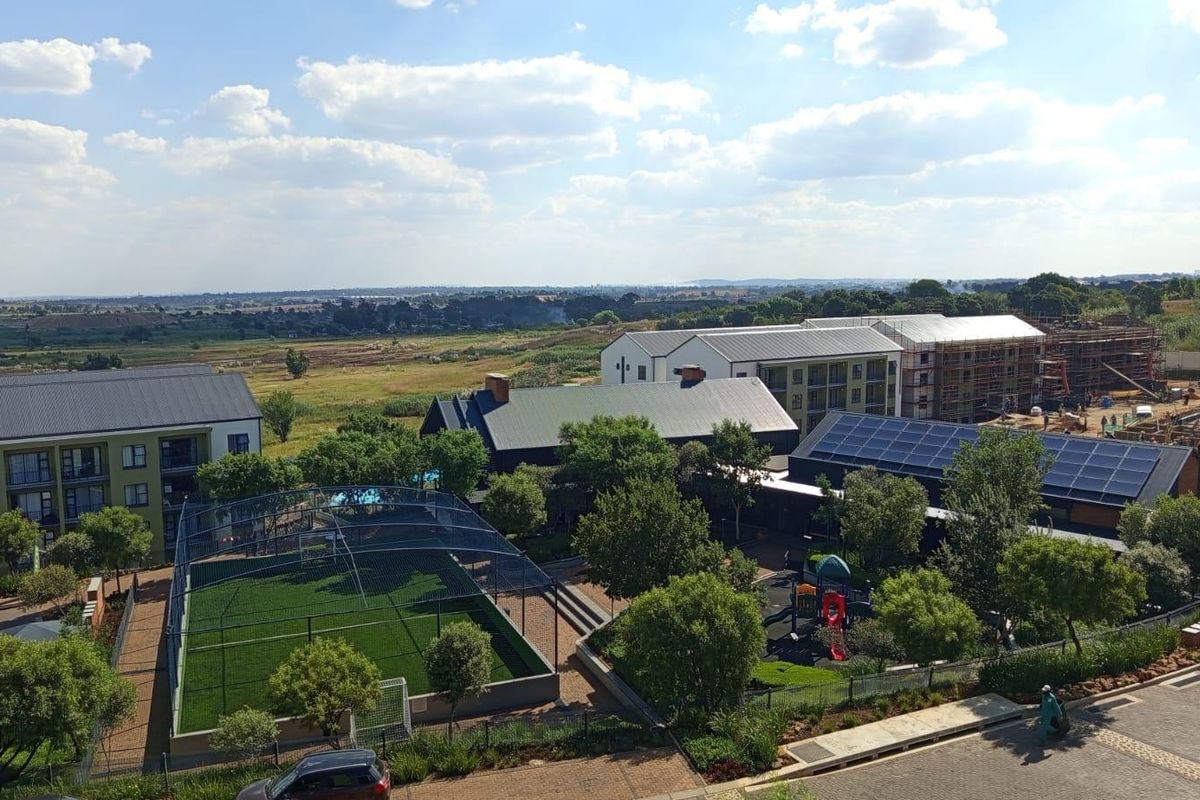 An elevated aerial view of an apartment complex featuring a sports court, playground, landscaped grounds, and buildings with solar panel installations.