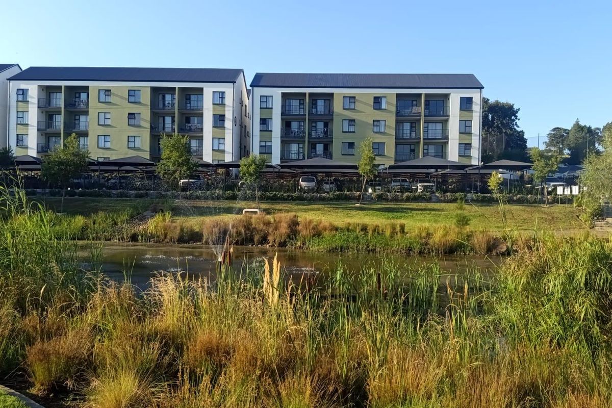 Exterior view of a modern apartment complex featuring landscaped gardens, a central water feature, and covered parking facilities.